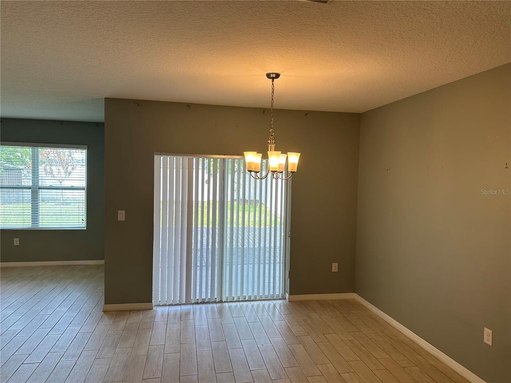 A dining area features tile flooring, a chandelier, and sliding glass doors with vertical blinds — 1519 DIAMOND LOOP DRIVE, KISSIMMEE, FL
