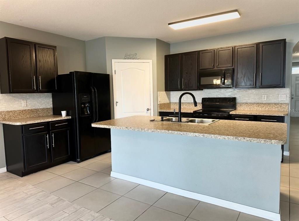A kitchen features dark wood cabinets, granite countertops, a central island, and black appliances — 1519 DIAMOND LOOP DRIVE, KISSIMMEE, FL