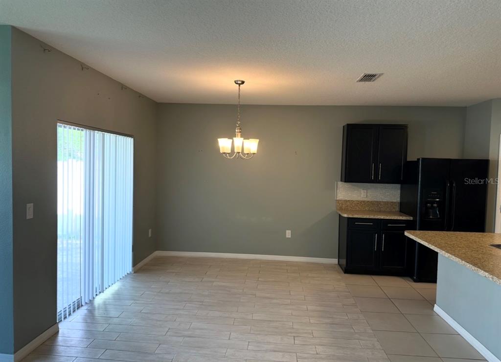 A dining area features gray walls, tile flooring, a chandelier, and dark kitchen cabinetry — 1519 DIAMOND LOOP DRIVE, KISSIMMEE, FL