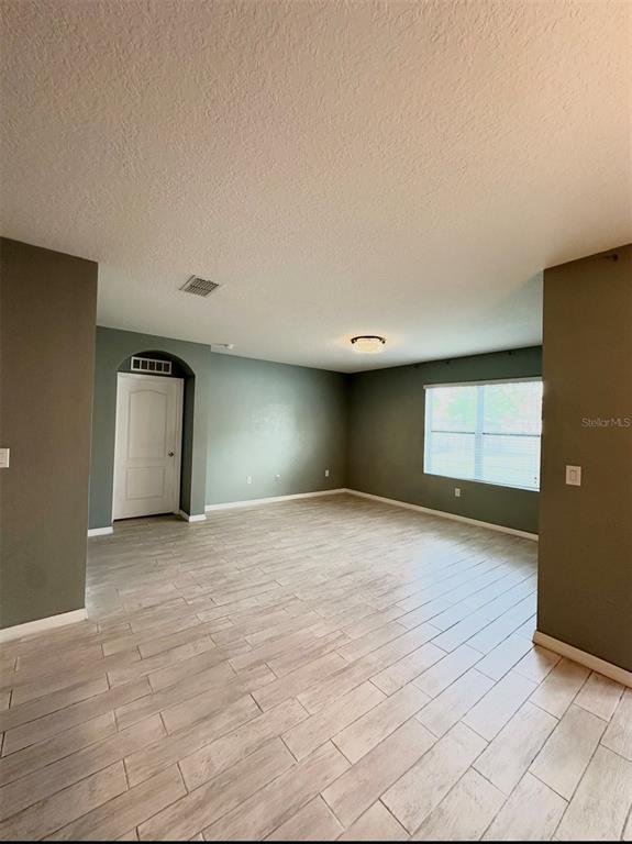 An empty room features light wood-look tile flooring, sage green walls, and a white door — 1519 DIAMOND LOOP DRIVE, KISSIMMEE, FL