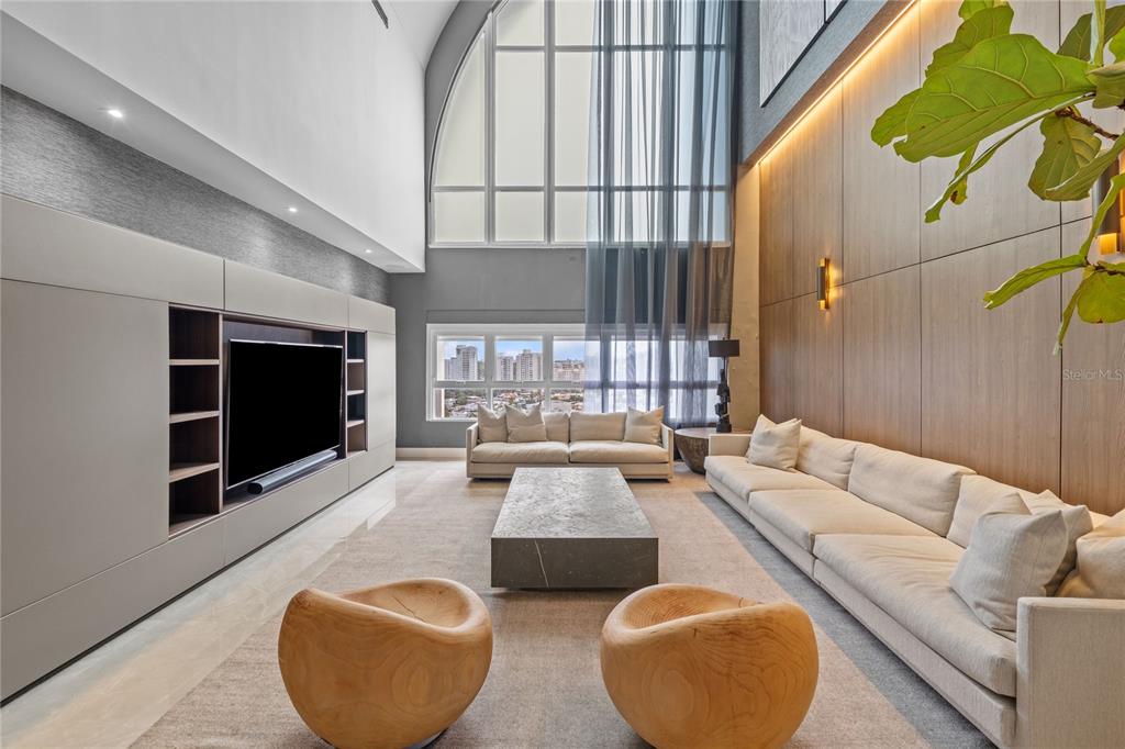 A modern living room features a double-height ceiling, wood-paneled wall, and large arched windows — 105 ORTEGON AVENUE UNIT PH1, GUAYNABO, PR