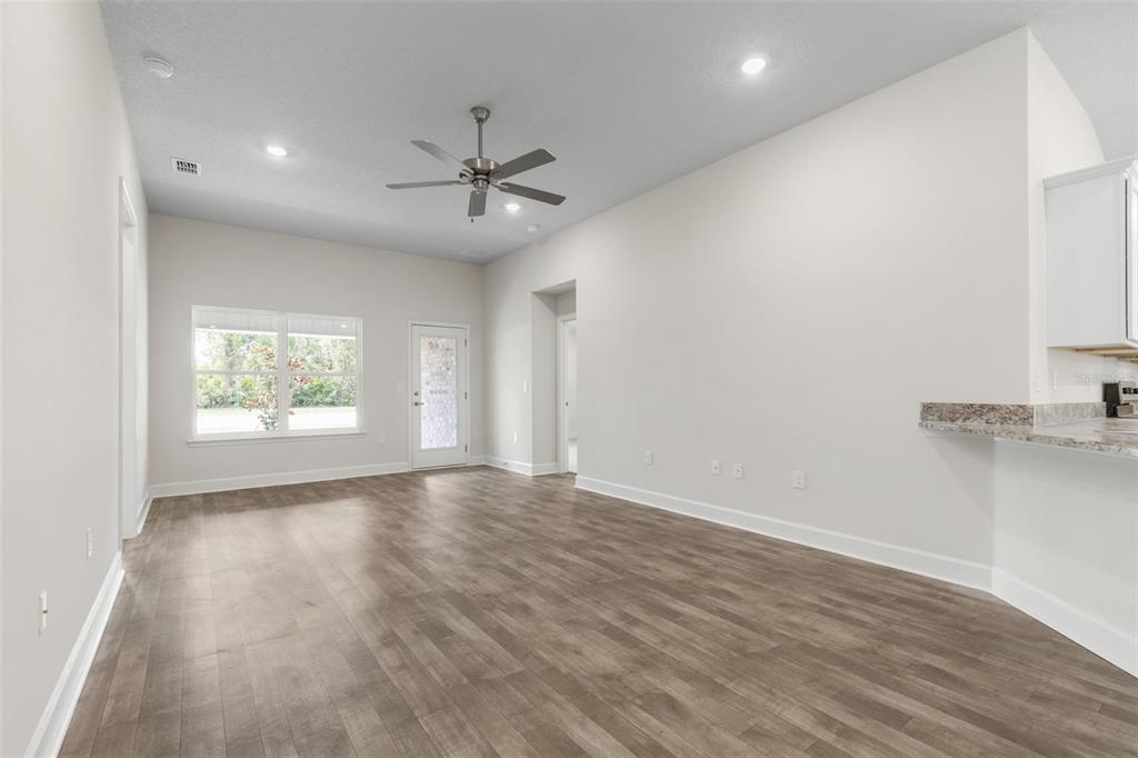An empty living room with wood-look flooring, a ceiling fan, and a kitchen breakfast bar — 7 ZIRCON COURT, PALM COAST, FL