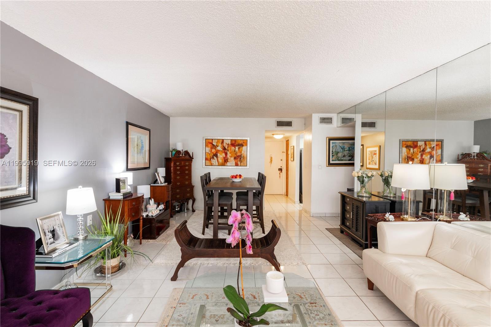A living and dining area features white tile floors, a mirrored wall, and neutral furniture — 1440 Brickell Bay Dr # 203, Miami FL 33131, MIAMI, FL