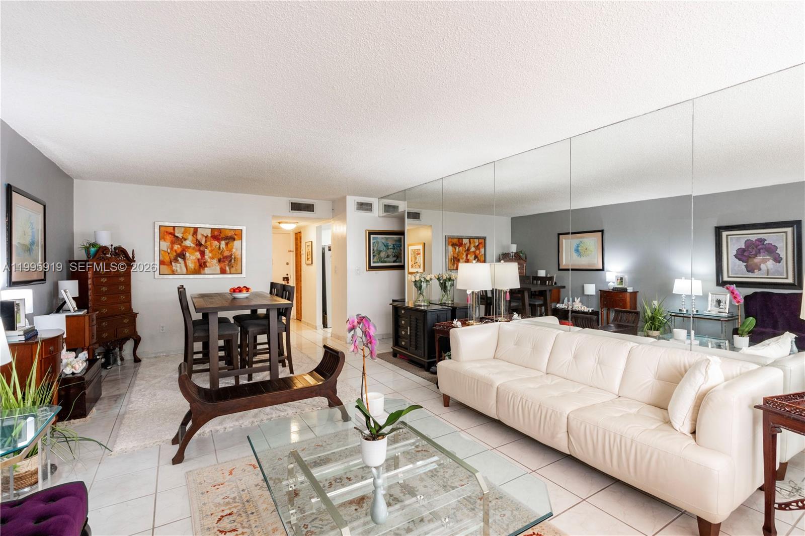 A living and dining area features white tile floors, a white sofa, and mirrored walls — 1440 Brickell Bay Dr # 203, Miami FL 33131, MIAMI, FL