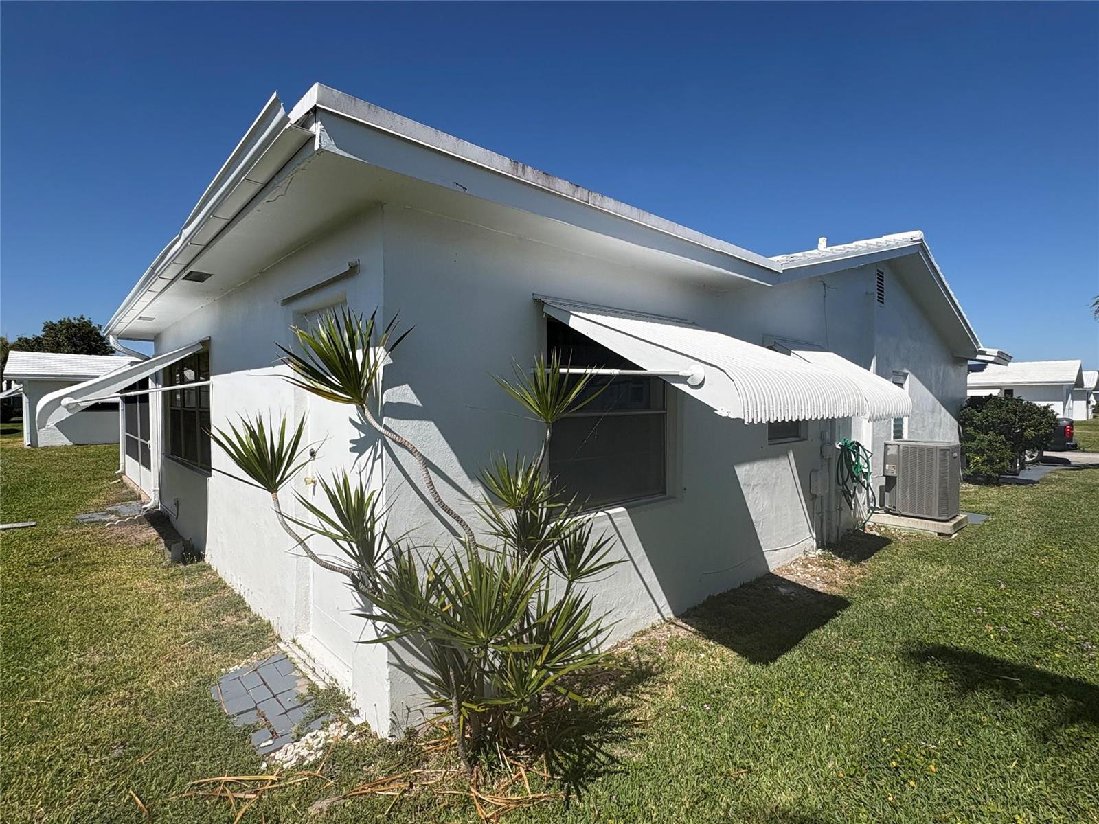 A white, single-story house exterior features metal window awnings and a small palm plant — 2392 SW 13th Terrace, Boynton Beach FL 33426, BOYNTON BEACH, FL