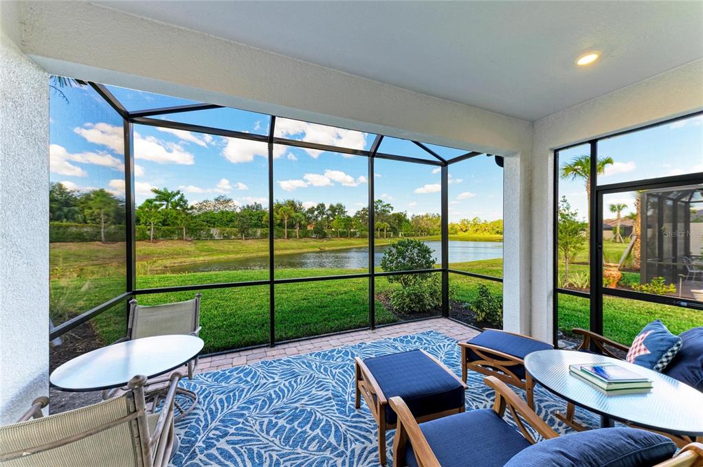 A screened-in patio features a blue patterned rug, outdoor furniture, and a view of a pond — 6017 MESA GLEN, BRADENTON, FL