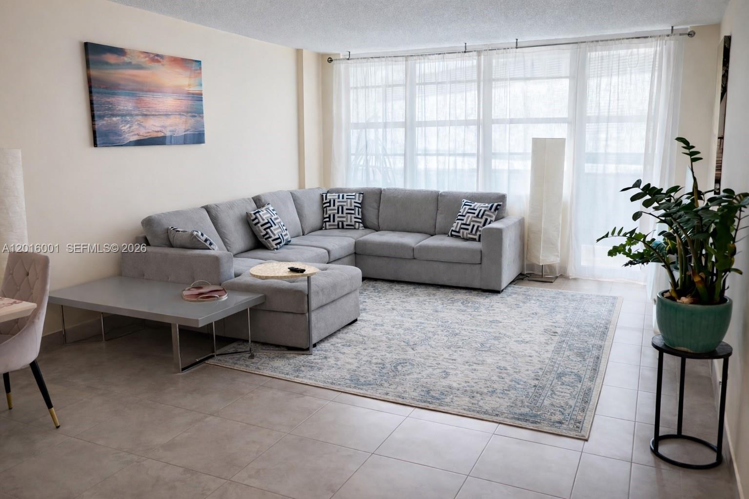 A living room features a gray sectional sofa, a patterned area rug, and floor-to-ceiling windows — 3725 S Ocean Dr # 1015, Hollywood FL 33019, HOLLYWOOD, FL