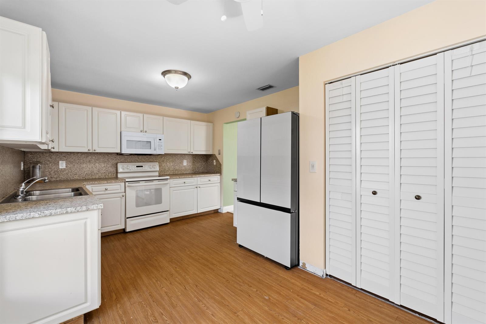 A kitchen features white cabinets, stainless steel appliances, granite countertops, and wood-look flooring — 3233 Perimeter Drive # 2511, FL 33467, FL
