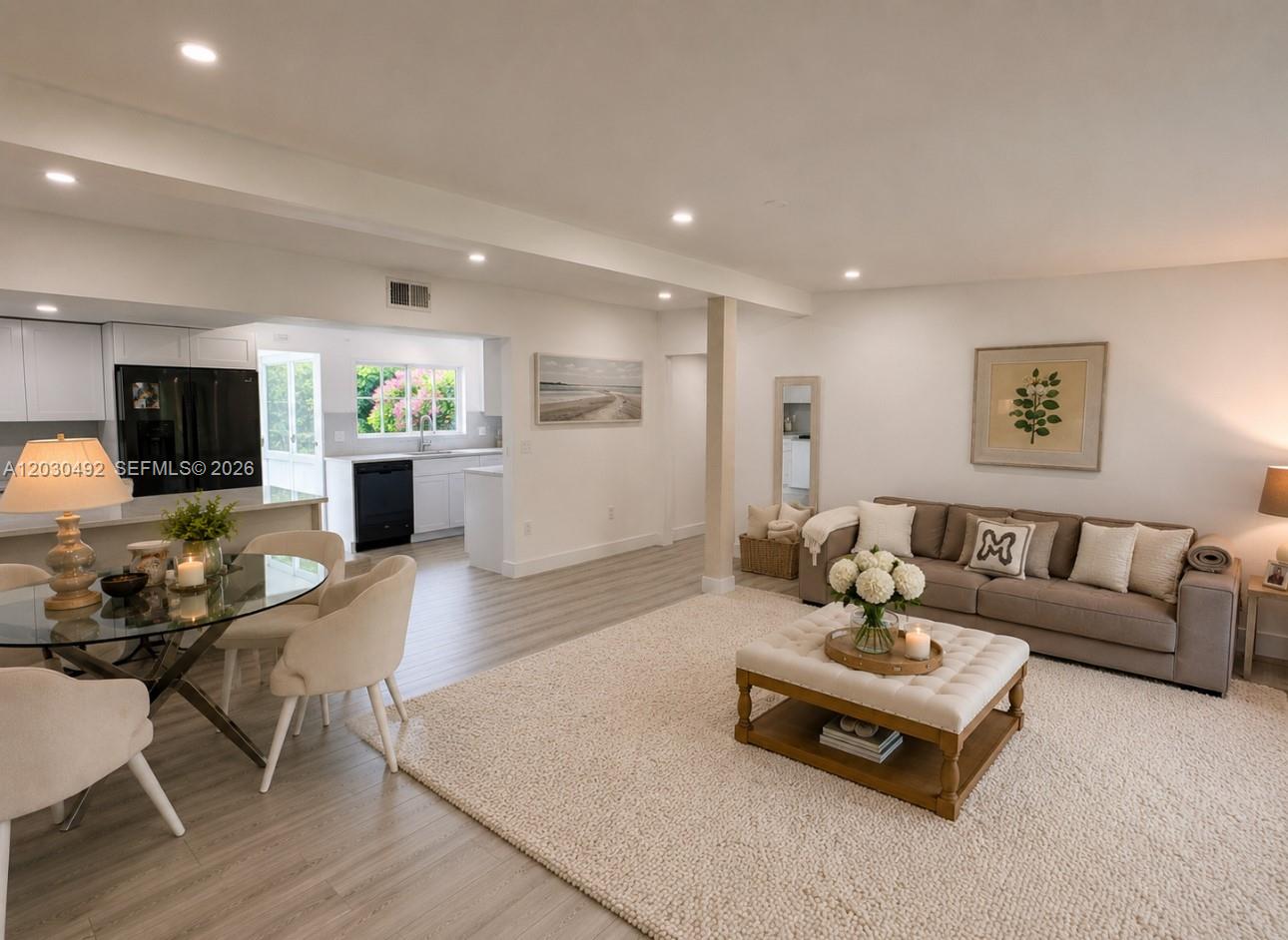 An open-concept living and dining area features light wood flooring, a neutral sofa, and kitchen — 1905 Alamanda Dr, North Miami FL 33181, NORTH MIAMI, FL