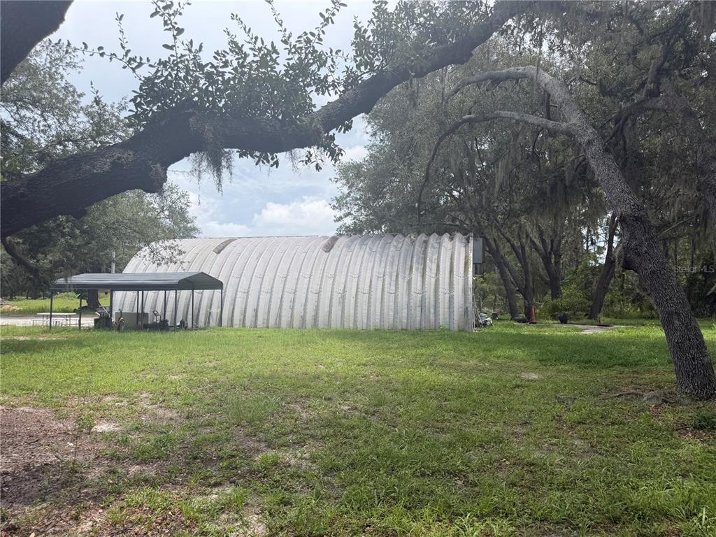 A large metal Quonset hut stands in a grassy yard under mature oak trees — 6828 STATE ROAD 33, CLERMONT, FL