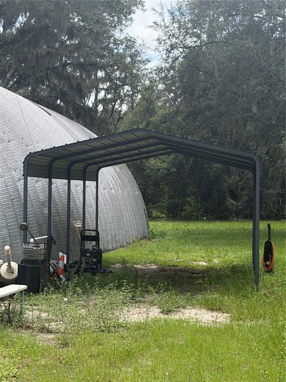 A metal carport stands on a grassy lot next to a large, curved metal building — 6828 STATE ROAD 33, CLERMONT, FL