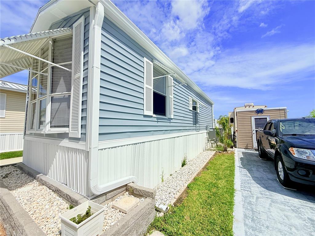 The exterior side of a light blue mobile home features white siding, shutters, and gravel landscaping — 2215 73RD STREET E UNIT 334, PALMETTO, FL