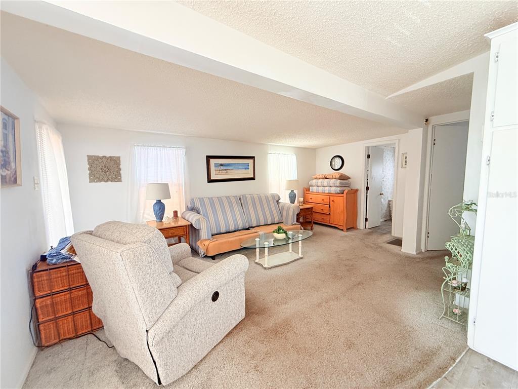 A living room features a striped sofa, a recliner, and beige carpeting under a beam — 2215 73RD STREET E UNIT 334, PALMETTO, FL