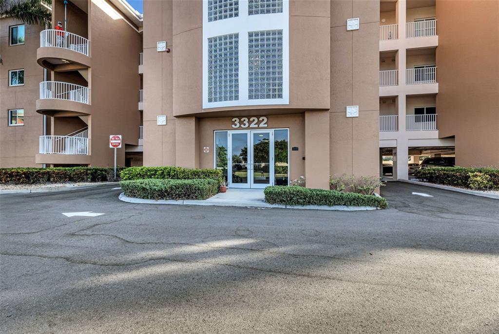 The exterior of a multi-story tan apartment building features a glass-paneled entrance labeled 3322 — 3322 PURPLE MARTIN DRIVE UNIT 126, PUNTA GORDA, FL