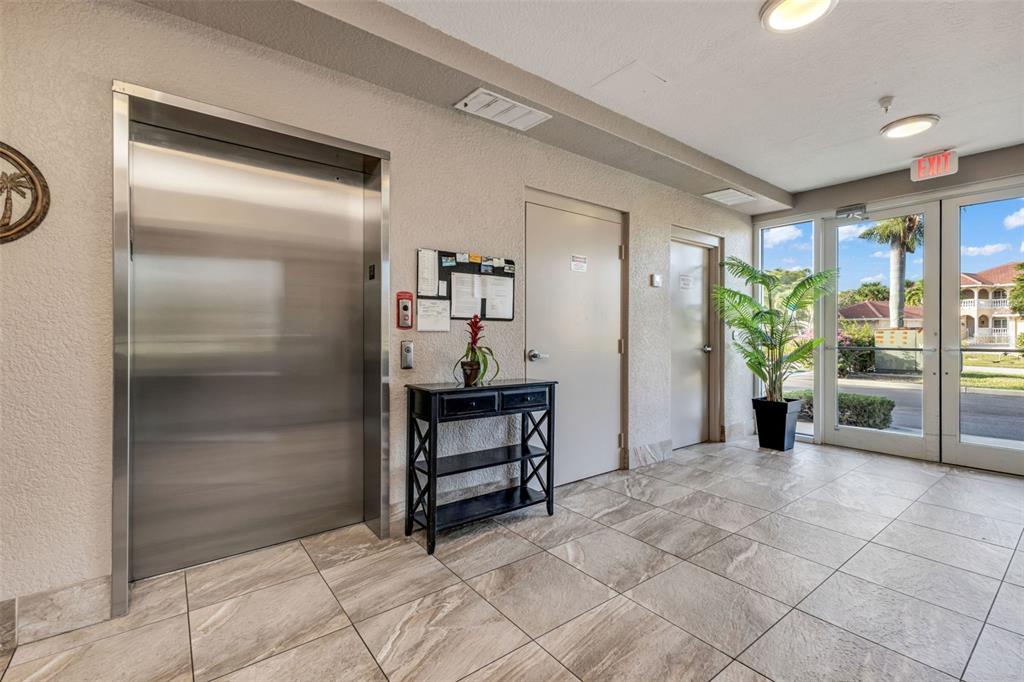 A lobby features a stainless steel elevator, a black console table, and glass exterior doors — 3322 PURPLE MARTIN DRIVE UNIT 126, PUNTA GORDA, FL