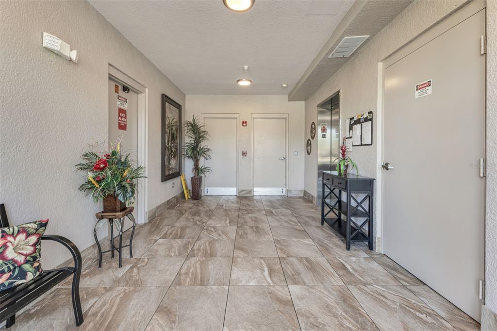 A tiled hallway features an elevator, several doors, a console table, and decorative plants — 3322 PURPLE MARTIN DRIVE UNIT 126, PUNTA GORDA, FL