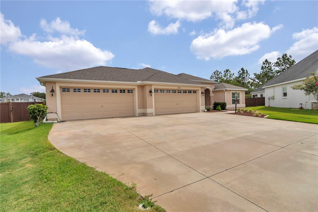 A beige single-story house features a three-car garage and a large concrete driveway — 11415 ZIMMERMAN PATH, OXFORD, FL