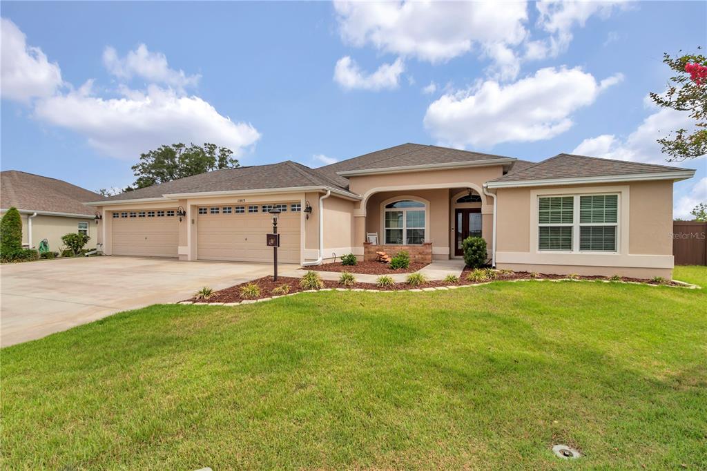 A single-story house with a three-car garage, tan stucco exterior, and a front lawn — 11415 ZIMMERMAN PATH, OXFORD, FL