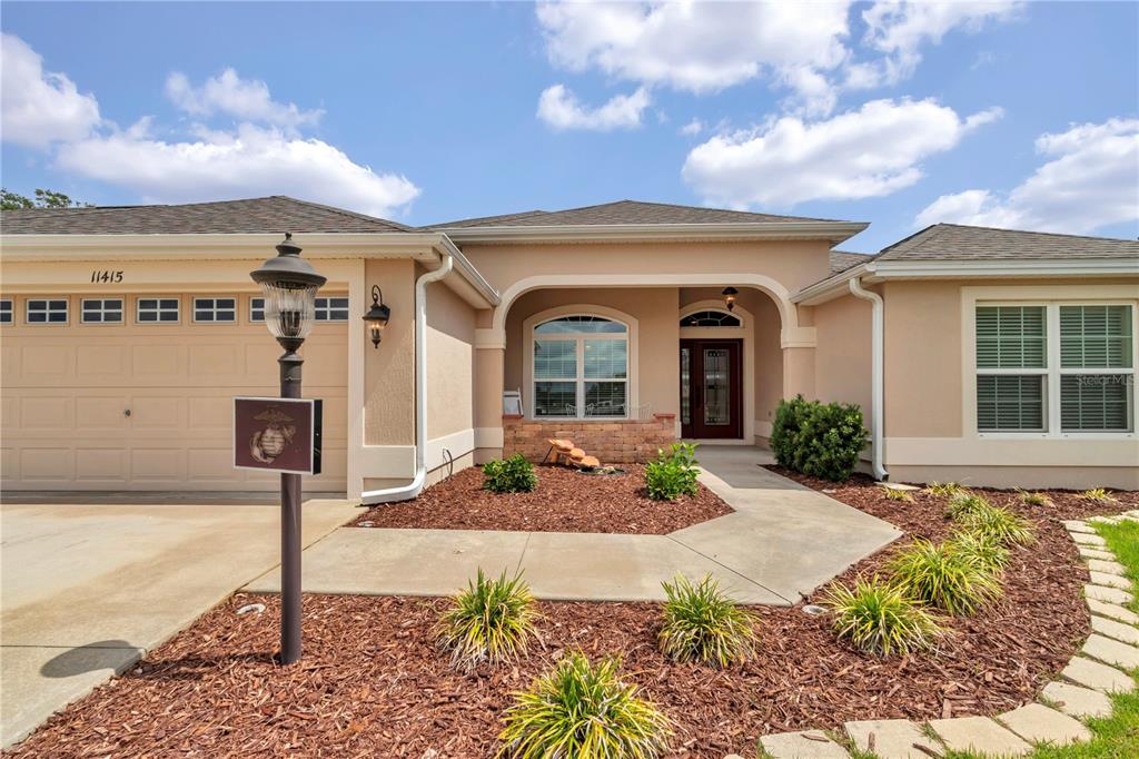 A single-story house with a beige stucco exterior, a two-car garage, and a front walkway — 11415 ZIMMERMAN PATH, OXFORD, FL