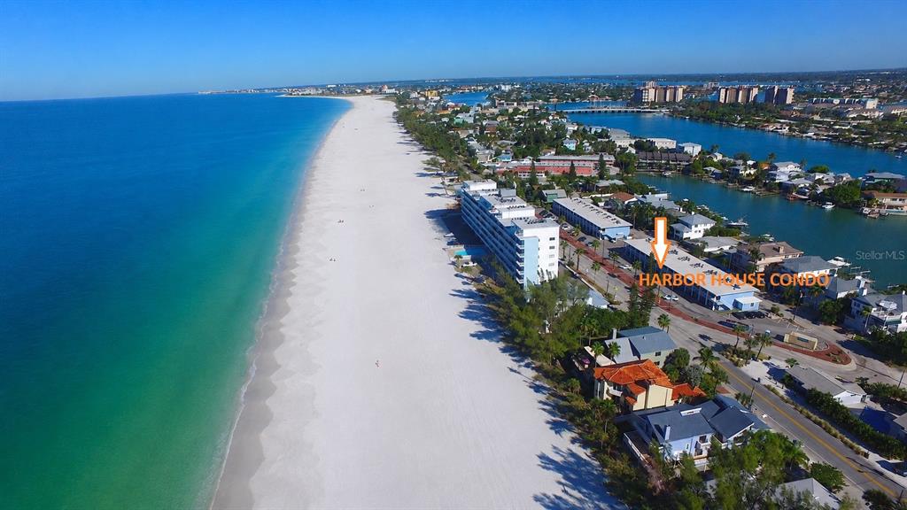 An aerial view shows a coastal beach, the ocean, and a multi-story condominium building — 8465 W GULF BOULEVARD UNIT 52, TREASURE ISLAND, FL