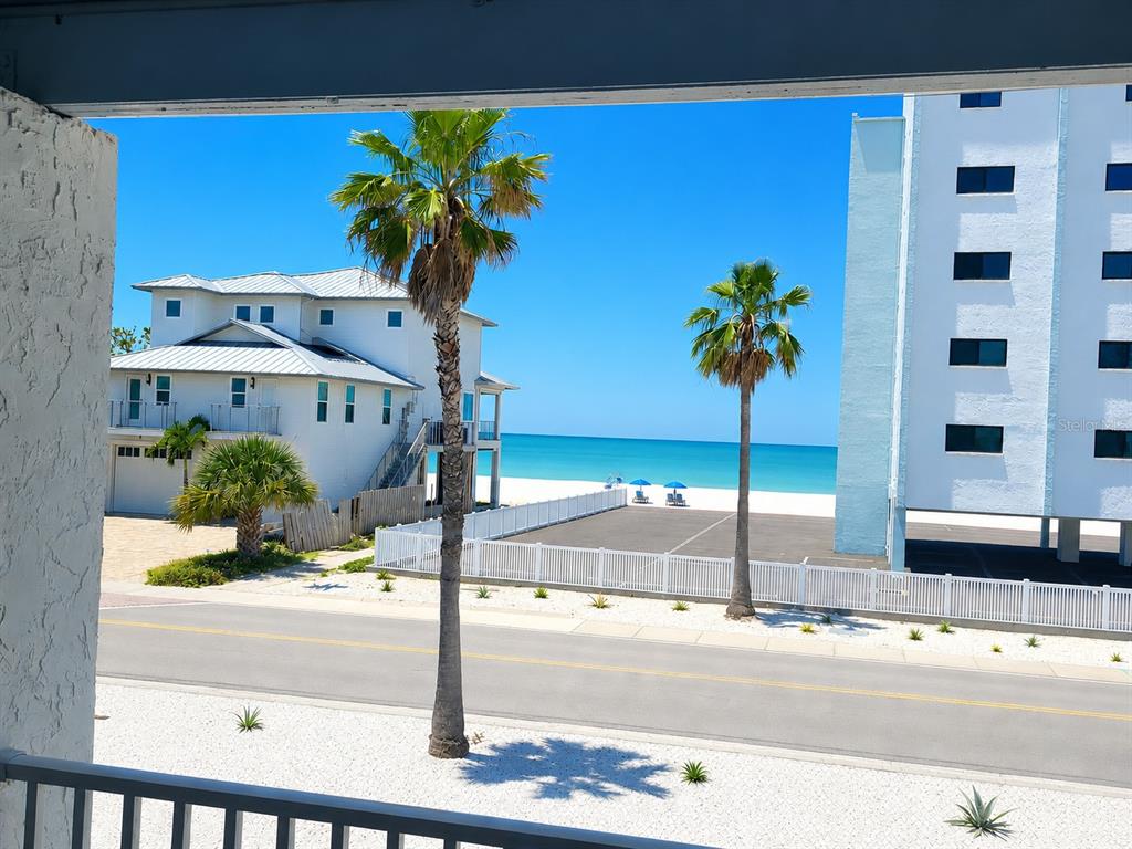 A view from a balcony overlooking a road, palm trees, a beach house, and the ocean — 8465 W GULF BOULEVARD UNIT 52, TREASURE ISLAND, FL