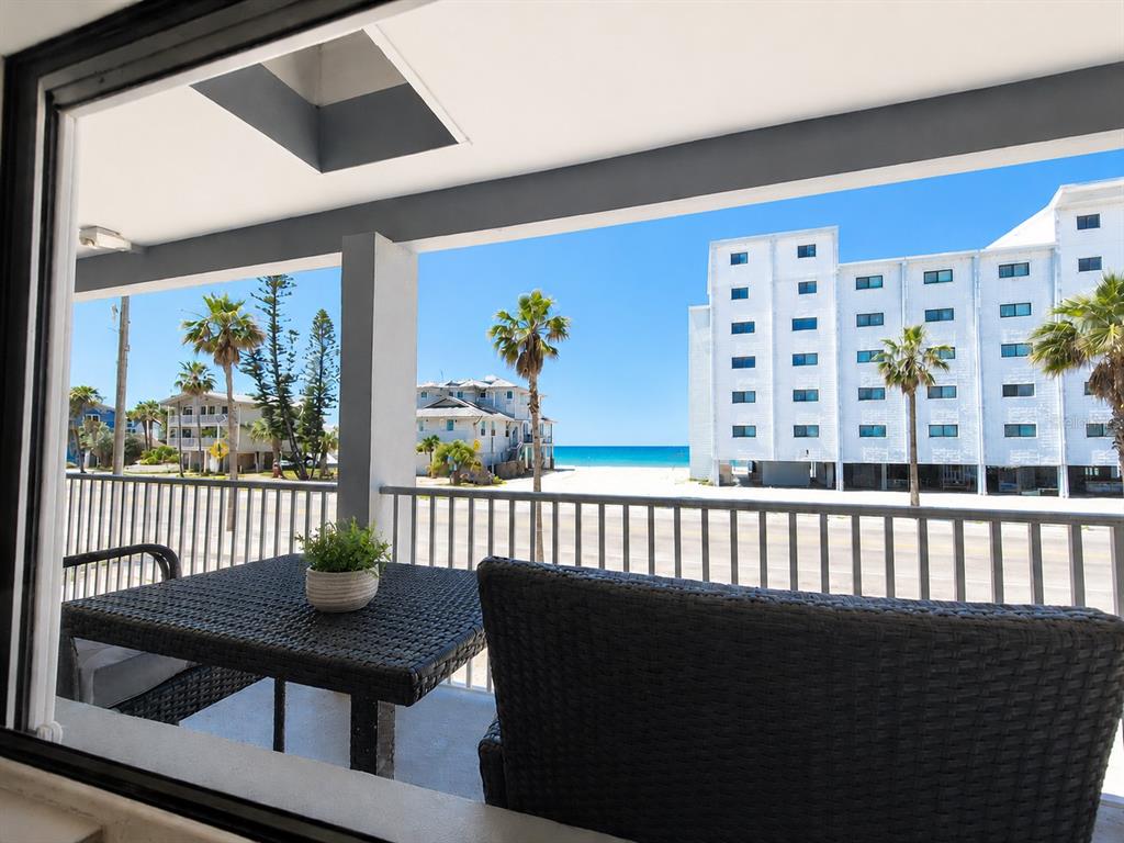 A balcony with outdoor furniture overlooks a beach, palm trees, and a large white building — 8465 W GULF BOULEVARD UNIT 52, TREASURE ISLAND, FL