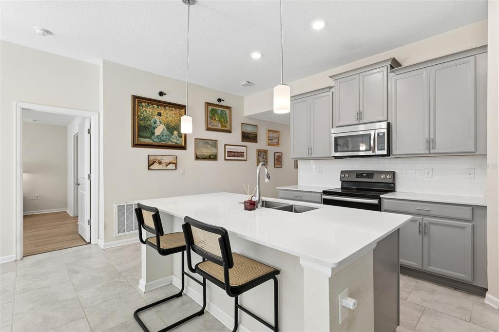 A kitchen with a white island, gray cabinets, stainless steel appliances, and a gallery wall — 4810 MAGNETITE LOOP, MOUNT DORA, FL