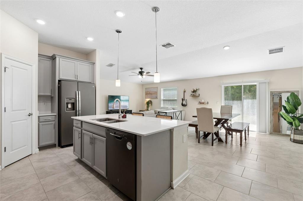 A modern kitchen with gray cabinets and a white island opens into a dining area — 4810 MAGNETITE LOOP, MOUNT DORA, FL