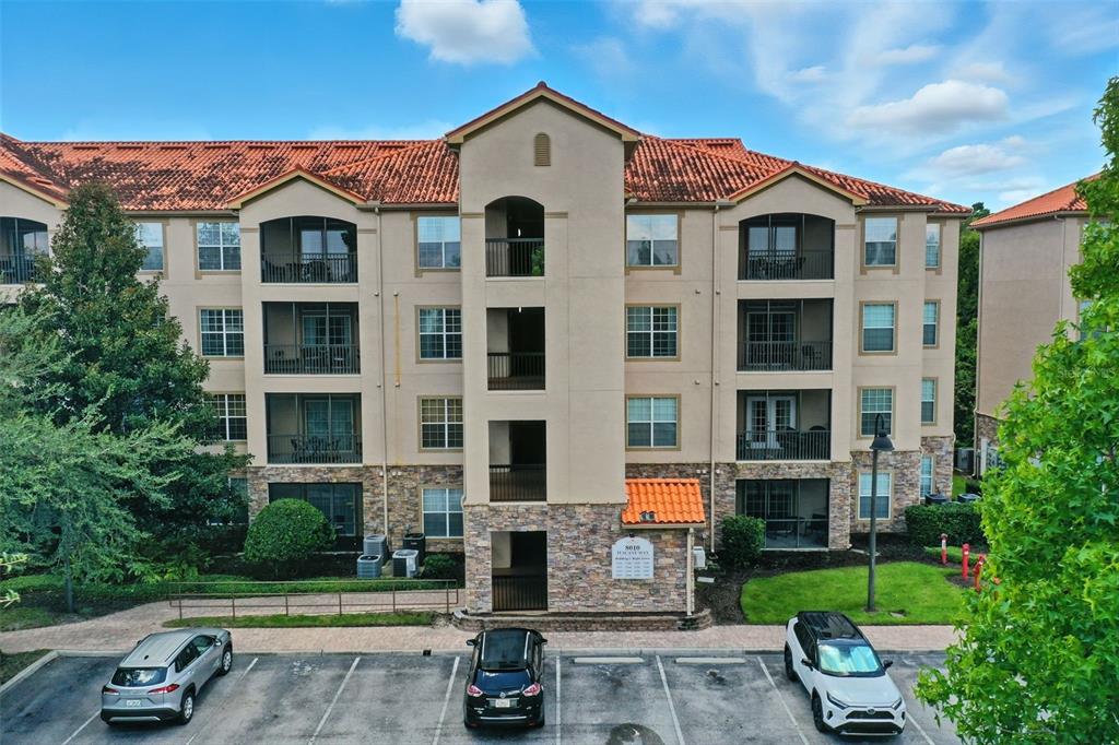 An exterior view of a multi-story apartment building with a stone facade and tiled roof — 8000 TUSCANY WAY UNIT 4405, DAVENPORT, FL