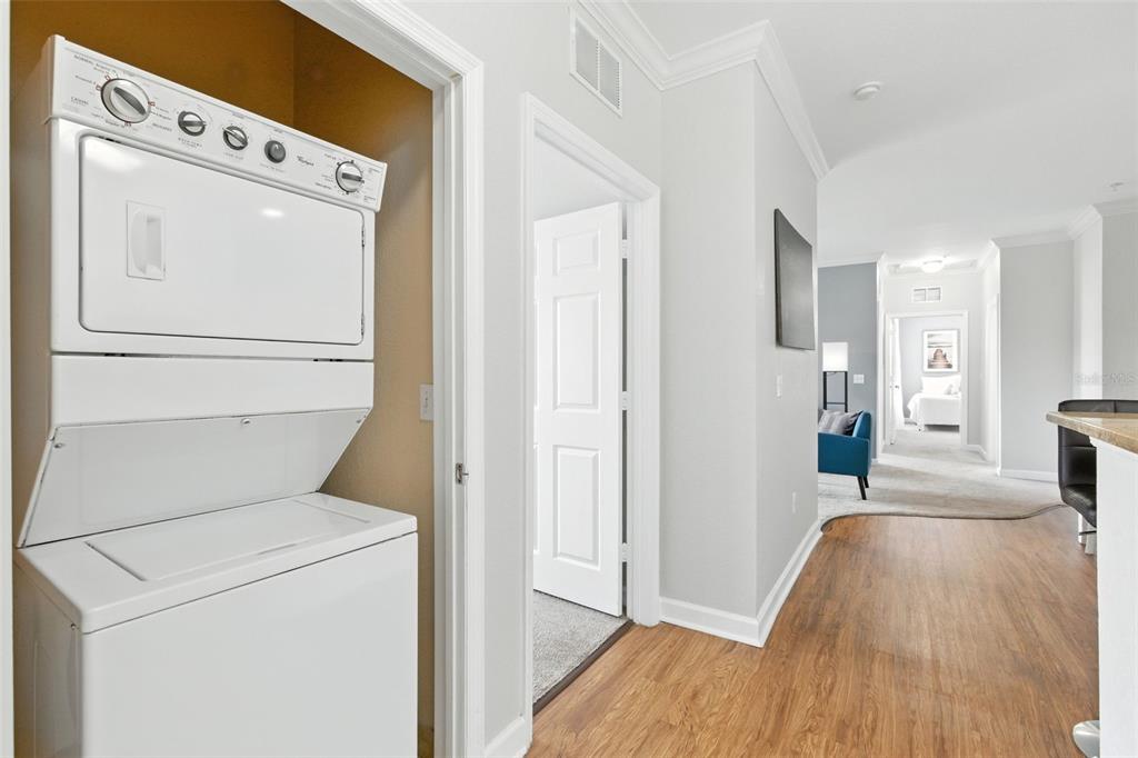 A stacked washer and dryer unit sits in a closet beside a hallway with wood flooring — 8000 TUSCANY WAY UNIT 4405, DAVENPORT, FL