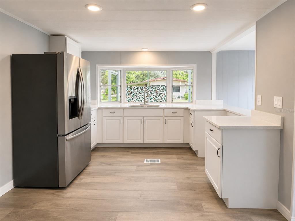 A kitchen features white cabinets, stainless steel appliances, light countertops, and wood-look flooring — 202 CALOOSA LAKE CIRCLE S, LAKE WALES, FL