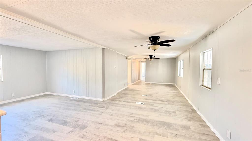An open-concept living area features light wood-look flooring, gray paneled walls, and two ceiling fans — 202 CALOOSA LAKE CIRCLE S, LAKE WALES, FL