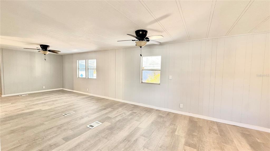An empty room features light wood-look flooring, white paneled walls, and two ceiling fans — 202 CALOOSA LAKE CIRCLE S, LAKE WALES, FL