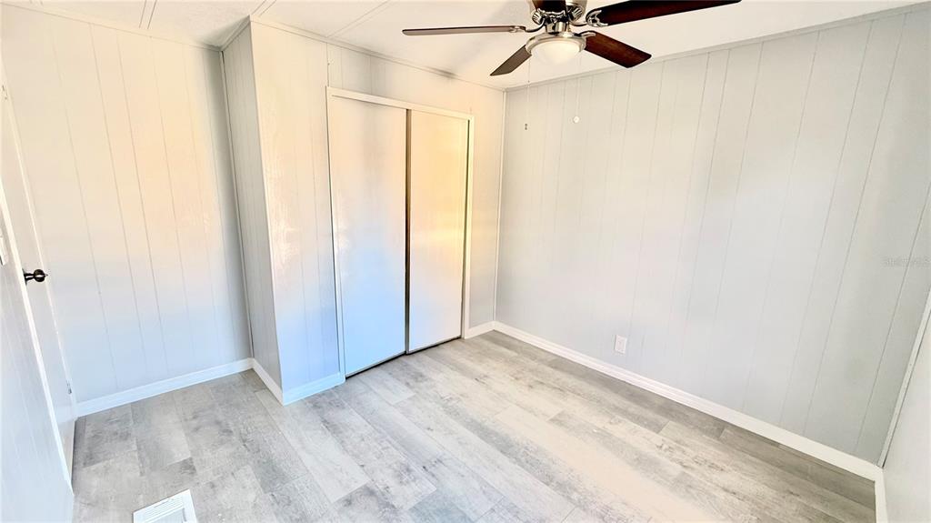 A bedroom with light-colored wood-look flooring, paneled walls, a ceiling fan, and sliding closet doors — 202 CALOOSA LAKE CIRCLE S, LAKE WALES, FL