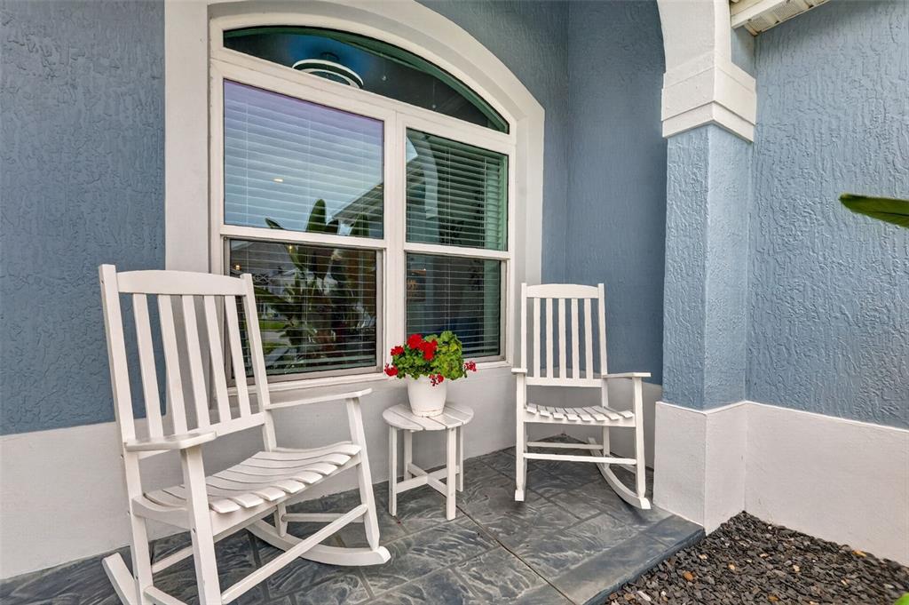 Two white rocking chairs and a small table sit on a blue-walled front porch — 6328 MERHOTTEIN LOOP, THE VILLAGES, FL