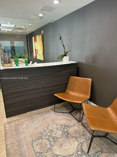 A reception area features a dark wood desk, two tan chairs, and a patterned rug — 95 Merrick Way # 710, Coral Gables FL 33134, CORAL GABLES, FL