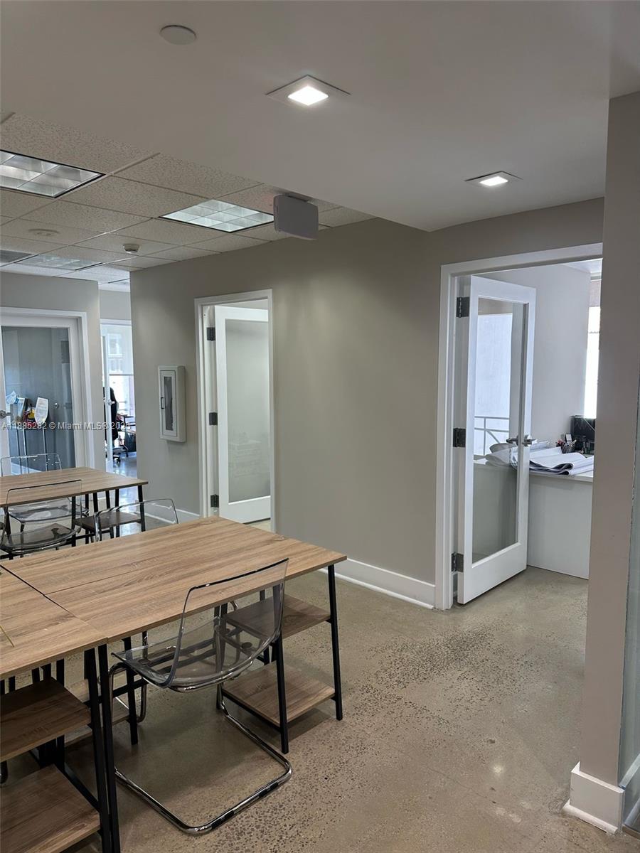 An office space features wood-topped tables, clear chairs, and multiple doorways leading to other rooms — 95 Merrick Way # 710, Coral Gables FL 33134, CORAL GABLES, FL