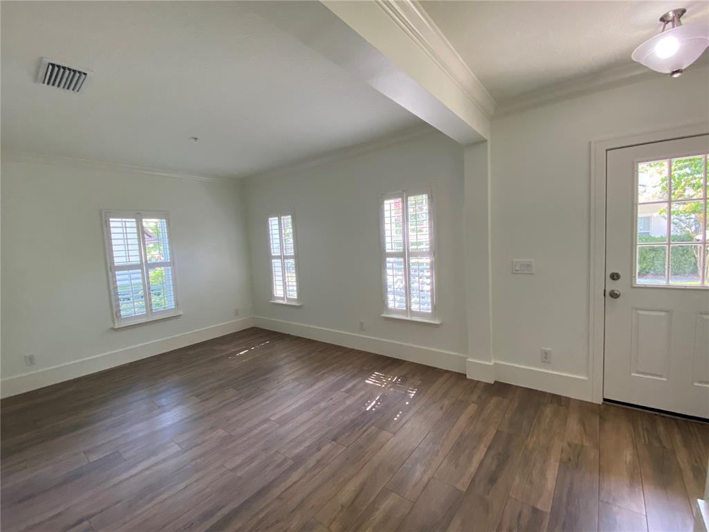An empty room features white walls, wood-look flooring, three windows with shutters, and a door — 2856 KEMPER AVENUE, ORLANDO, FL