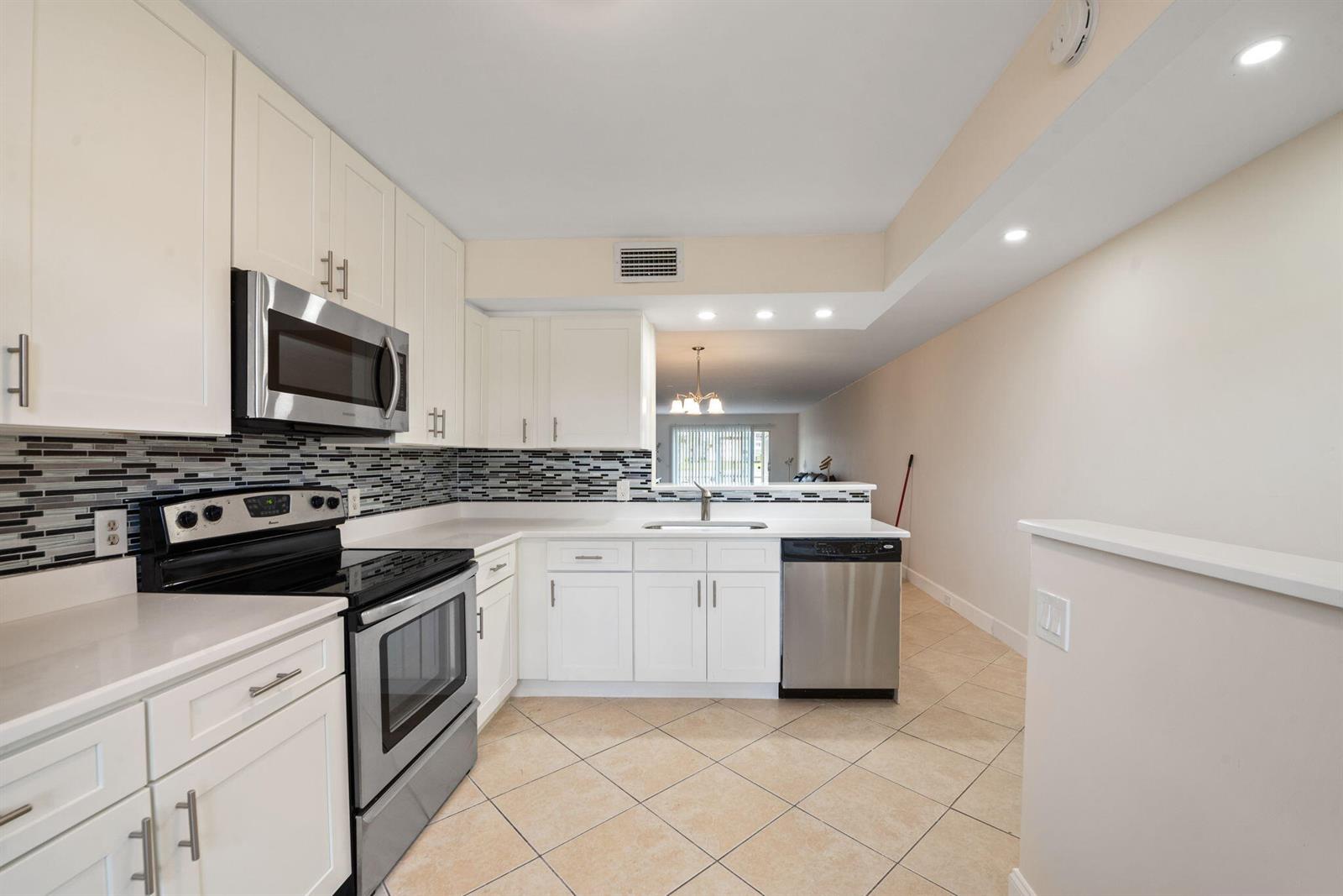 A kitchen features white cabinetry, stainless steel appliances, a tiled backsplash, and light-colored flooring — 1090 Guildford E # 1090, Boca Raton FL 33434, BOCA RATON, FL