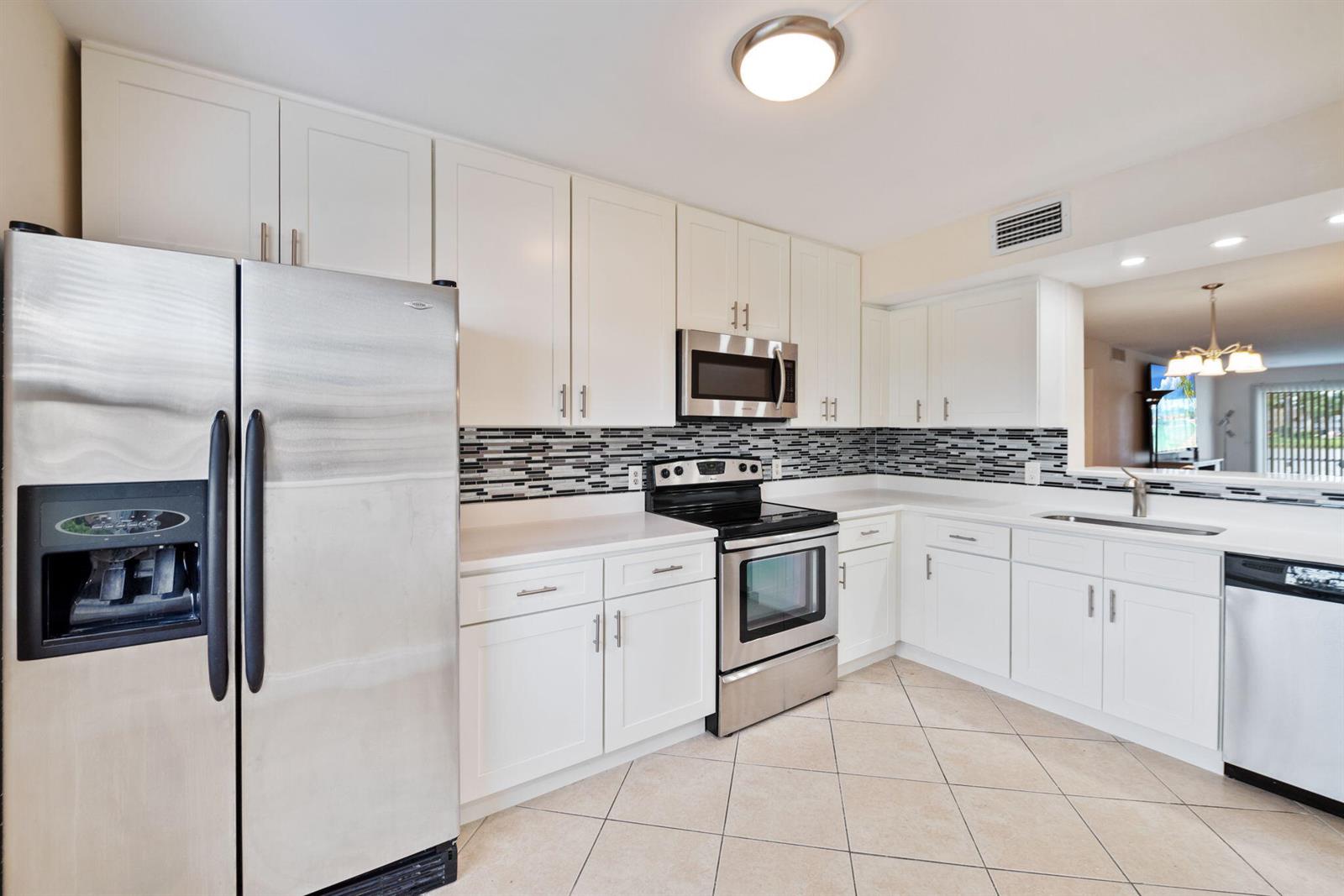 A kitchen features white cabinets, stainless steel appliances, a tiled backsplash, and light-colored floor tiles — 1090 Guildford E # 1090, Boca Raton FL 33434, BOCA RATON, FL