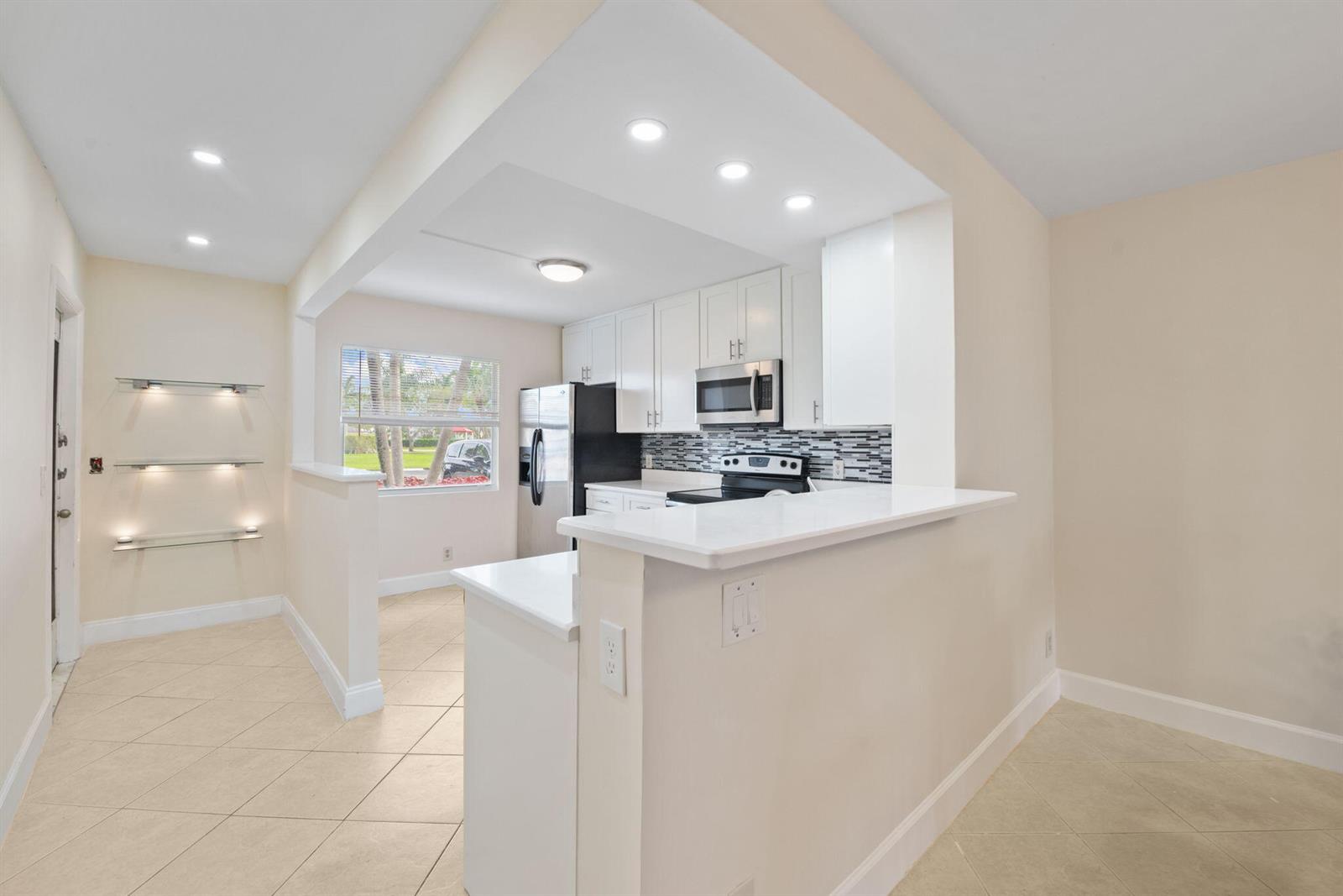 A kitchen with white cabinets, stainless steel appliances, and a breakfast bar overlooks a dining area — 1090 Guildford E # 1090, Boca Raton FL 33434, BOCA RATON, FL