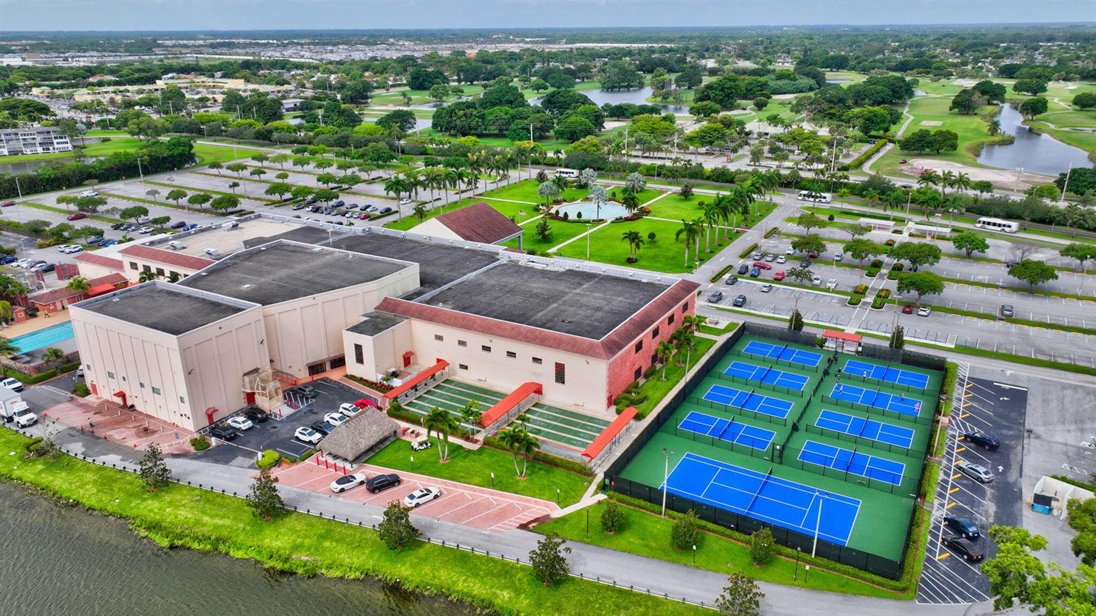 An aerial view shows a large building, tennis courts, parking lots, and surrounding green space — 1090 Guildford E # 1090, Boca Raton FL 33434, BOCA RATON, FL