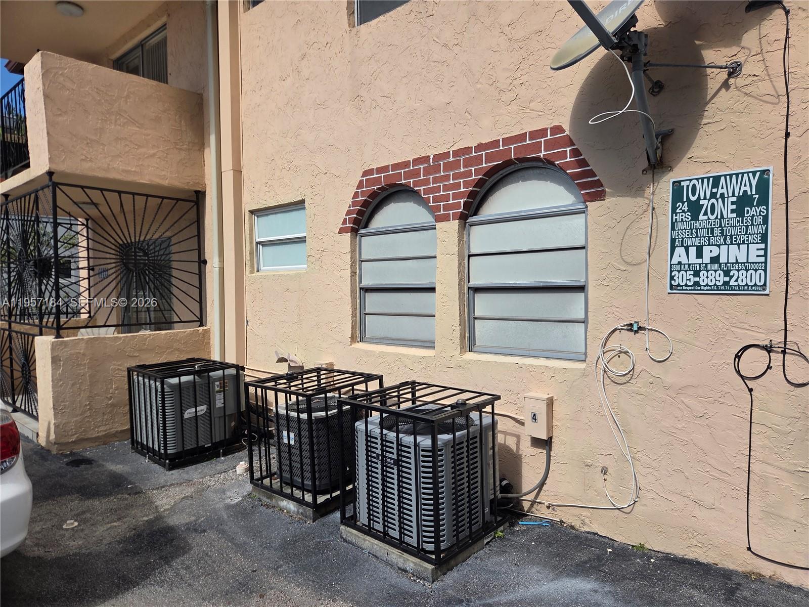 The exterior of a building features three air conditioning units in cages and two arched windows — 6373 SW 8th St, Miami FL 33144, MIAMI, FL