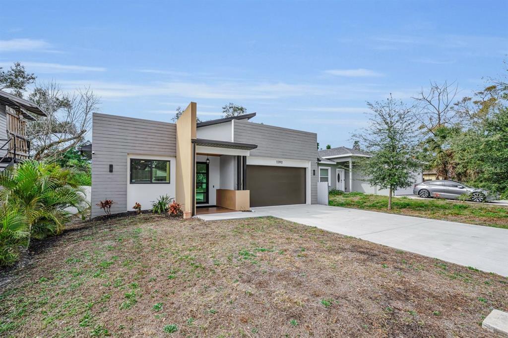 A modern single-story house with gray horizontal siding, a tan accent wall, and a concrete driveway — 1590 S WASHINGTON AVENUE, CLEARWATER, FL