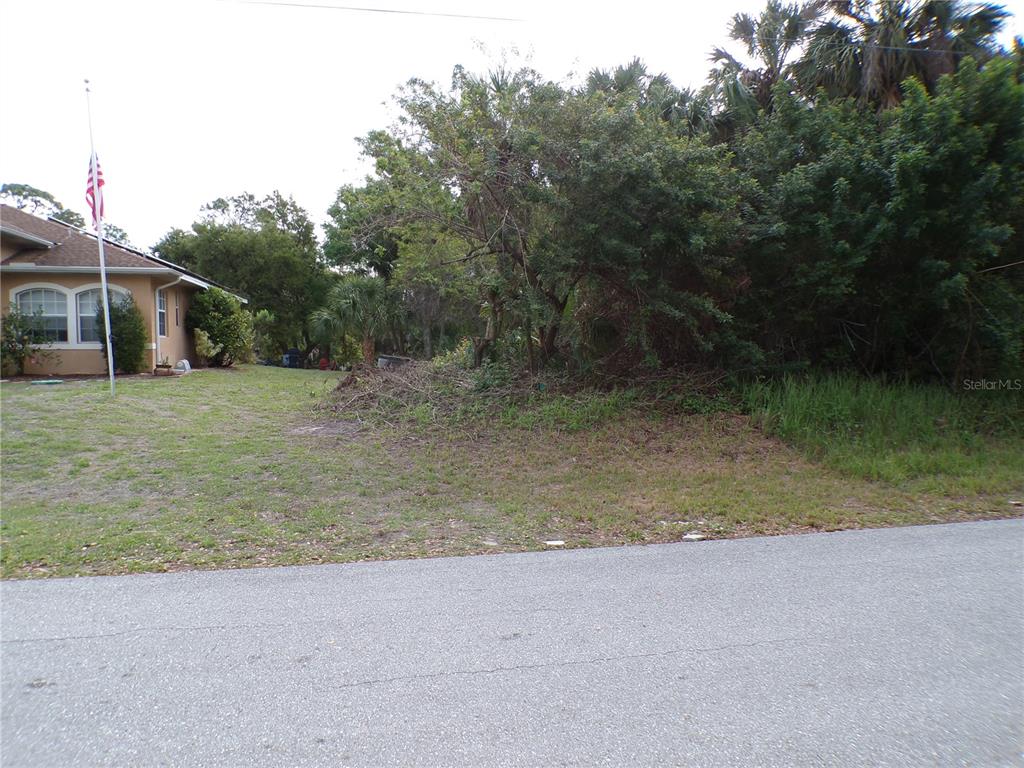 A grassy vacant lot sits next to a house with an American flag — 164 FERDON CIRCLE, PORT CHARLOTTE, FL