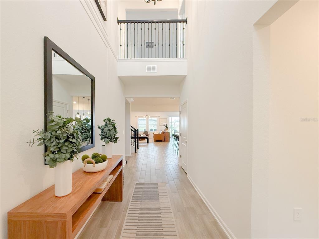 A bright entryway features a wooden console table, a large mirror, and a second-story balcony — 13993 TITLE WAY, WINTER GARDEN, FL