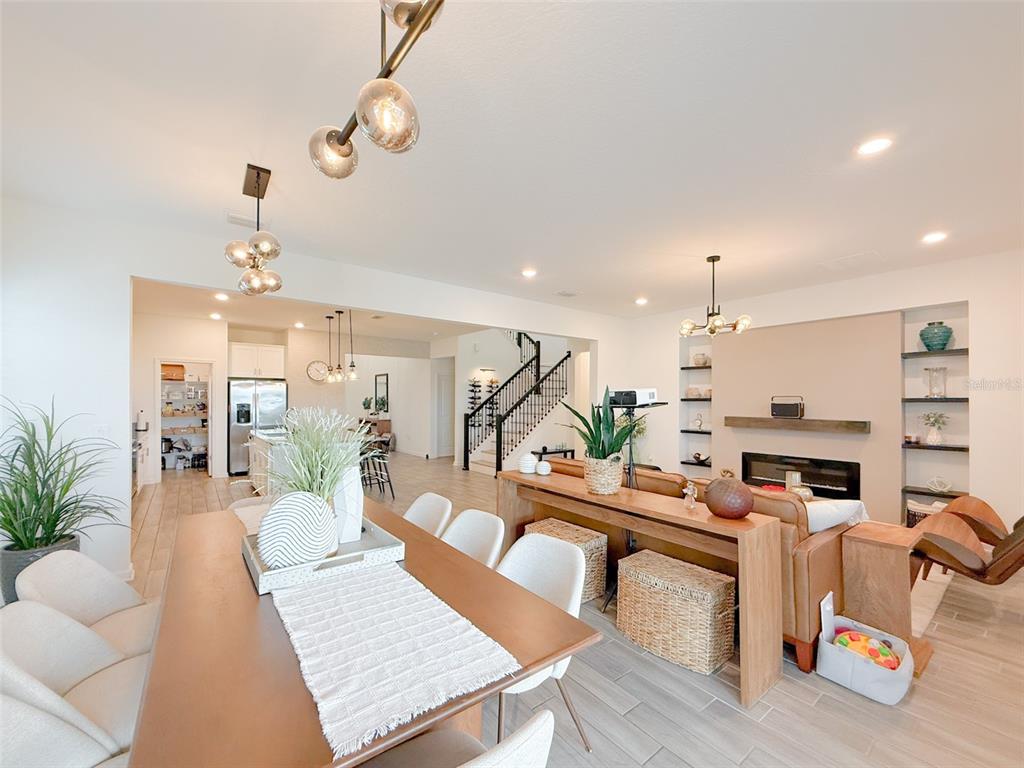 An open-concept living and dining area features a fireplace, staircase, and modern light fixtures — 13993 TITLE WAY, WINTER GARDEN, FL