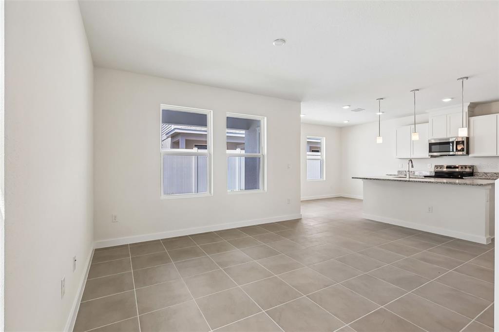 A bright, open-concept kitchen and dining area features white cabinetry, granite countertops, and tile flooring — 2692 MEADOW CREST DRIVE, ST CLOUD, FL