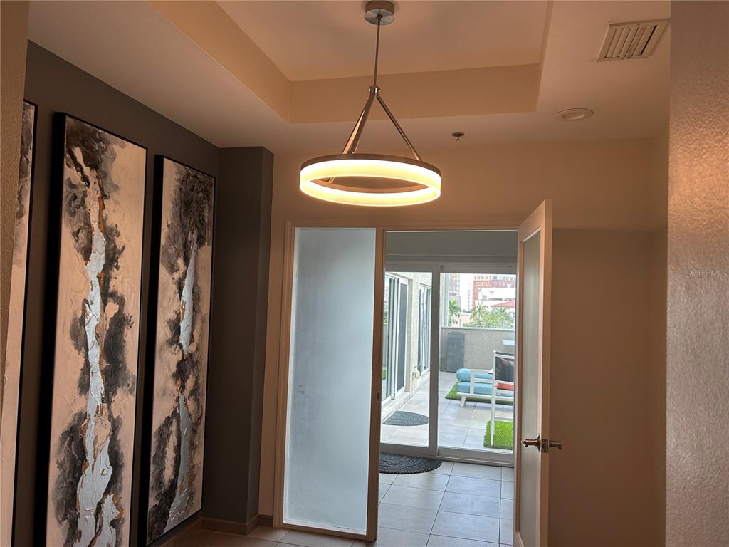 A modern foyer with a circular pendant light leads to an outdoor patio through glass doors — 1345 2ND STREET UNIT C, SARASOTA, FL