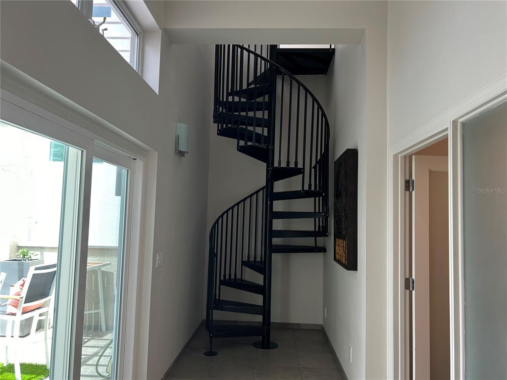 A black metal spiral staircase stands in a tiled hallway next to a glass sliding door — 1345 2ND STREET UNIT C, SARASOTA, FL